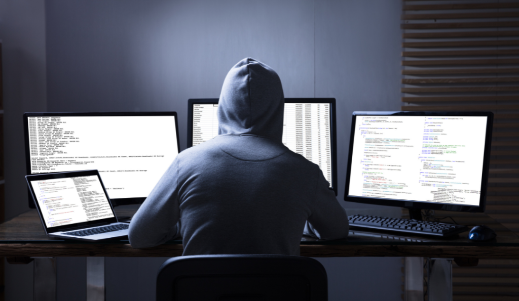 Guy wearing a hoodie sitting in front of computers.