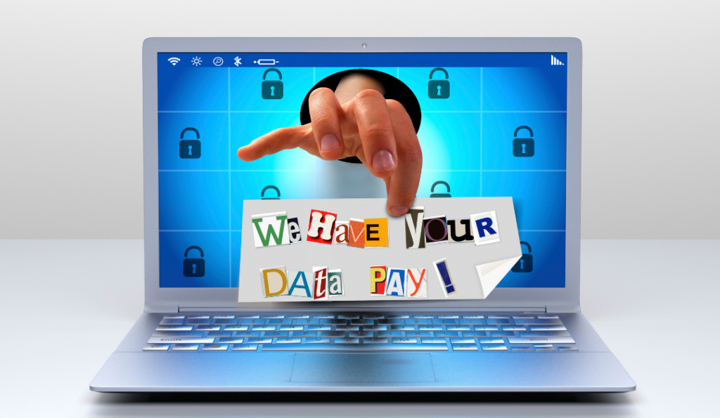Laptop with a hand coming out of the screen holding a ransom note.